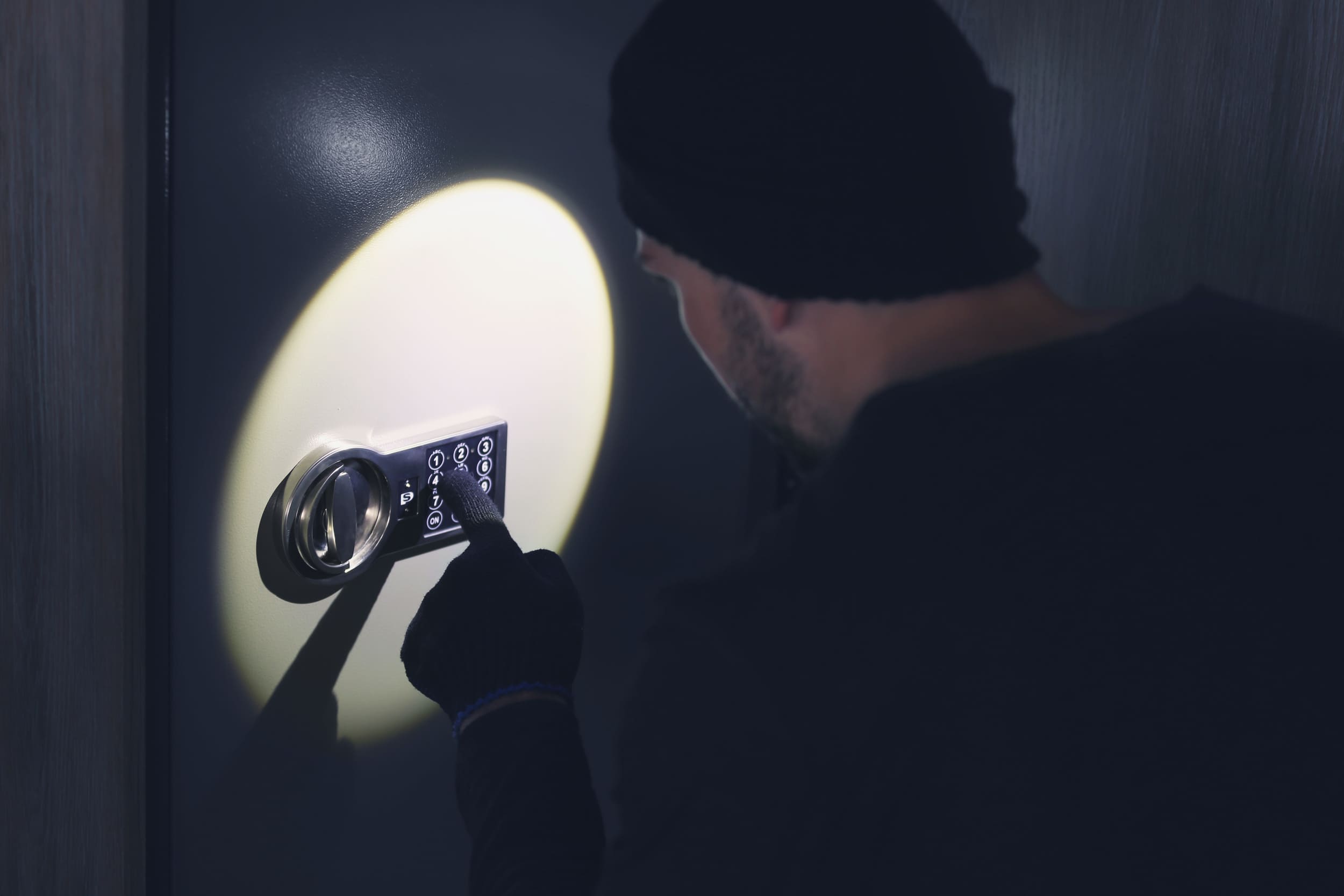 Burglar dressed in black cracks a safe by the light of a torch